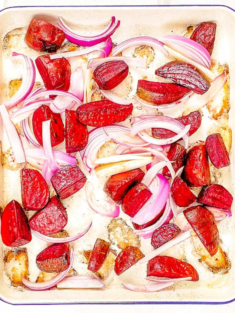 Beets and onions roasted on a baking sheet.