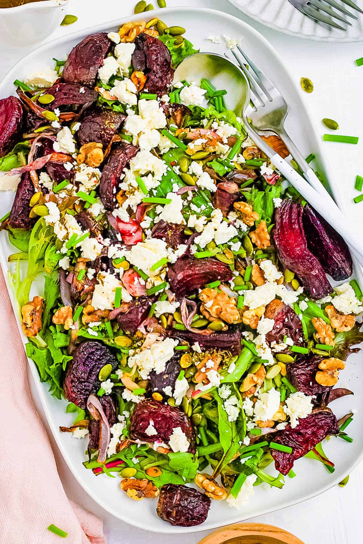 Roasted beetroot and feta salad with walnuts and mixed greens, served on a large white serving platter.