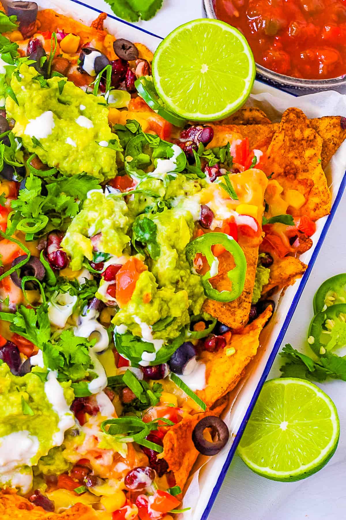 Vegetarian nachos piled with veggies, jalapenos, guacamole, sour cream, cheese, olives served on a white platter.