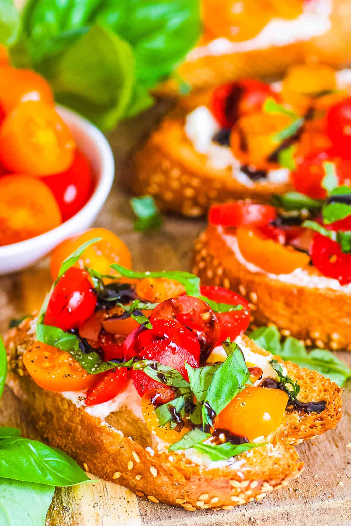 Bruschetta burrata toasts with tomatoes, basil, garlic, and a balsamic glaze served on a wooden cutting board.