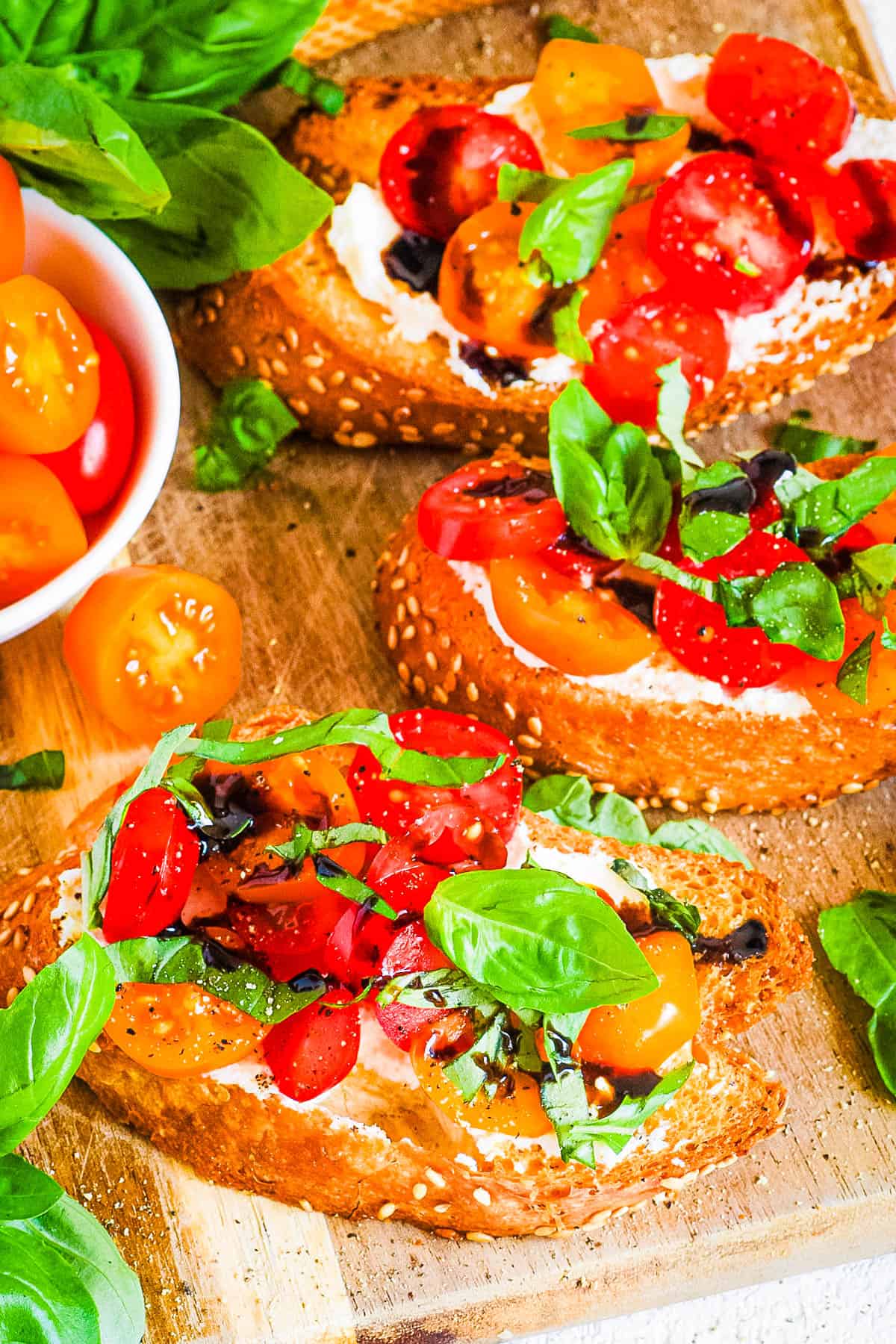 Bruschetta burrata toasts with tomatoes, basil, garlic, and a balsamic glaze served on a wooden cutting board.