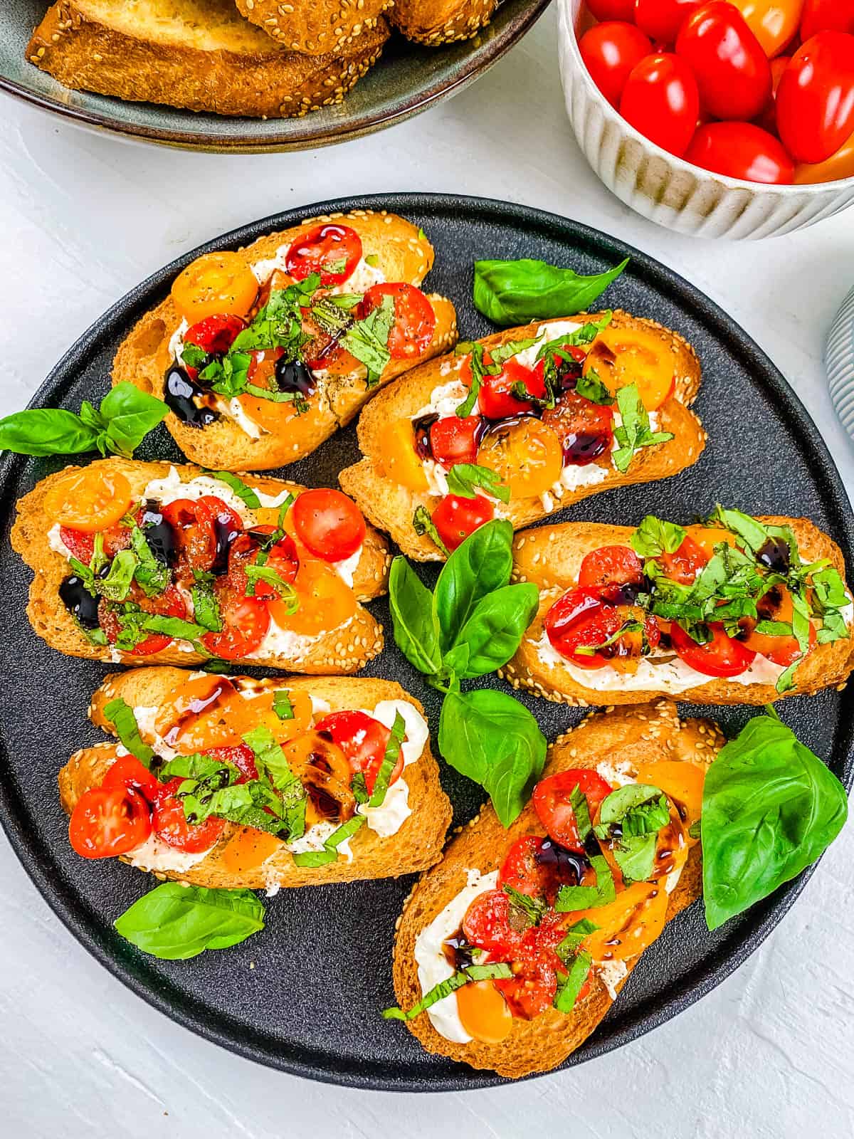 Bruschetta burrata toasts with tomatoes, basil, garlic, and a balsamic glaze served on a grey plate.