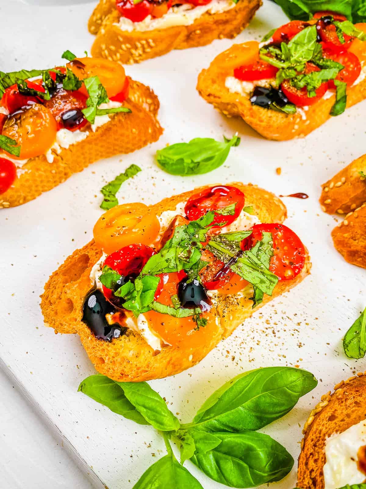 Burrata caprese crostini on a white cutting board.