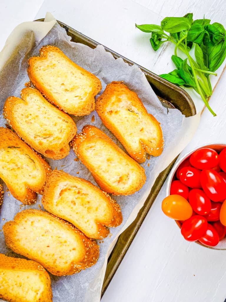 Sliced crostini on a baking sheet lined with parchment paper.