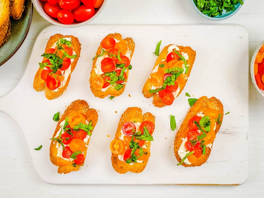 Crostini topped with burrata, tomatoes and basil on a cutting board.