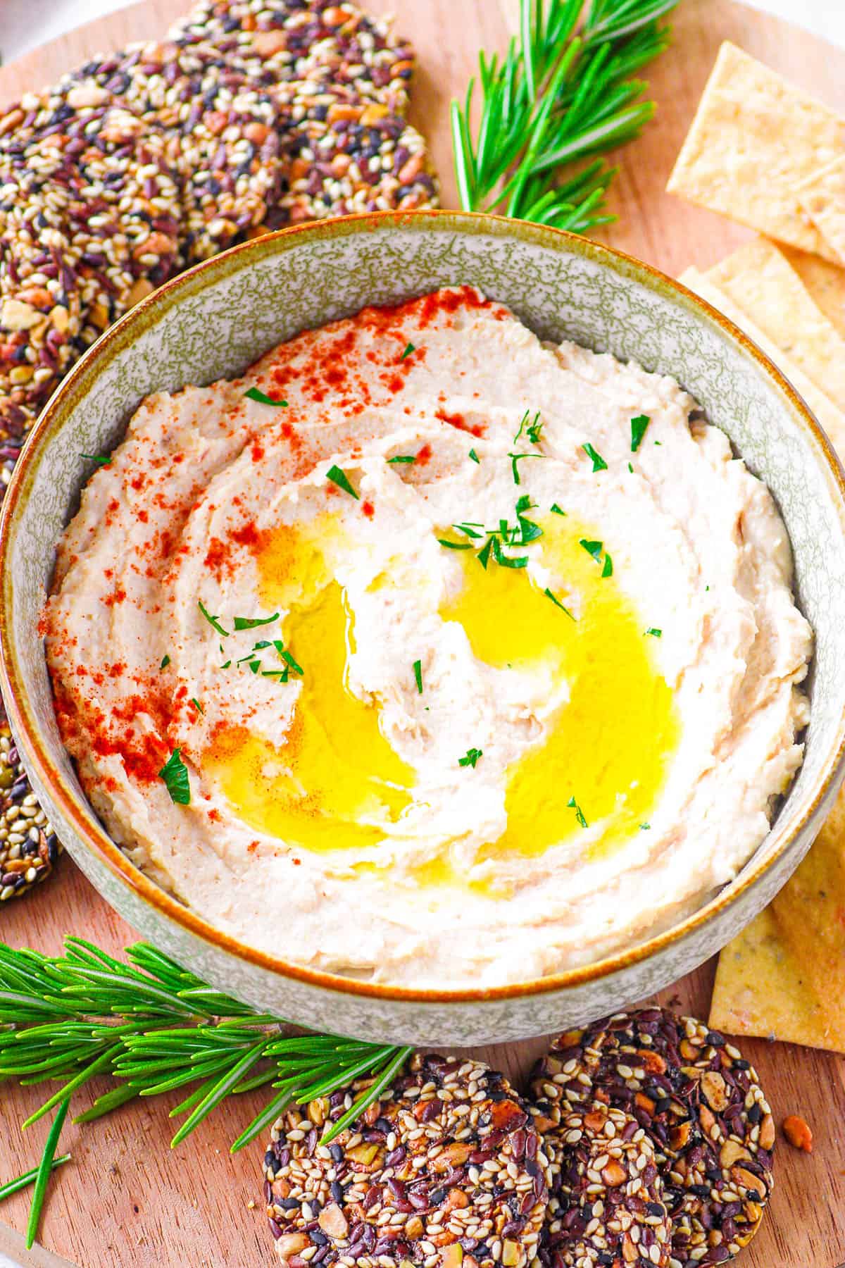 Easy butter bean hummus served in a bowl, with olive oil drizzled on top and crackers on the side.
