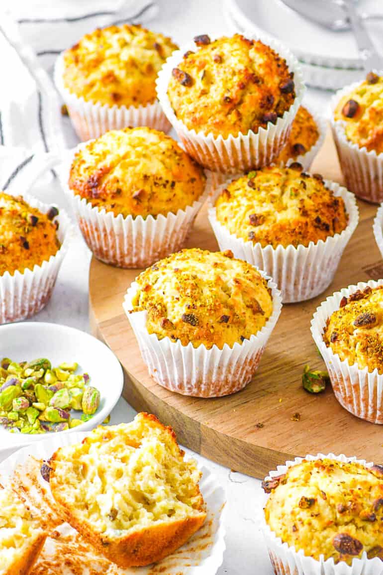 Homemade pistachio muffins stacked on a wooden cutting board.