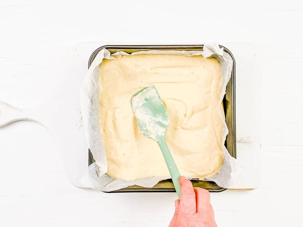 3 milk cake batter being spread in a baking tin lined with parchment paper.