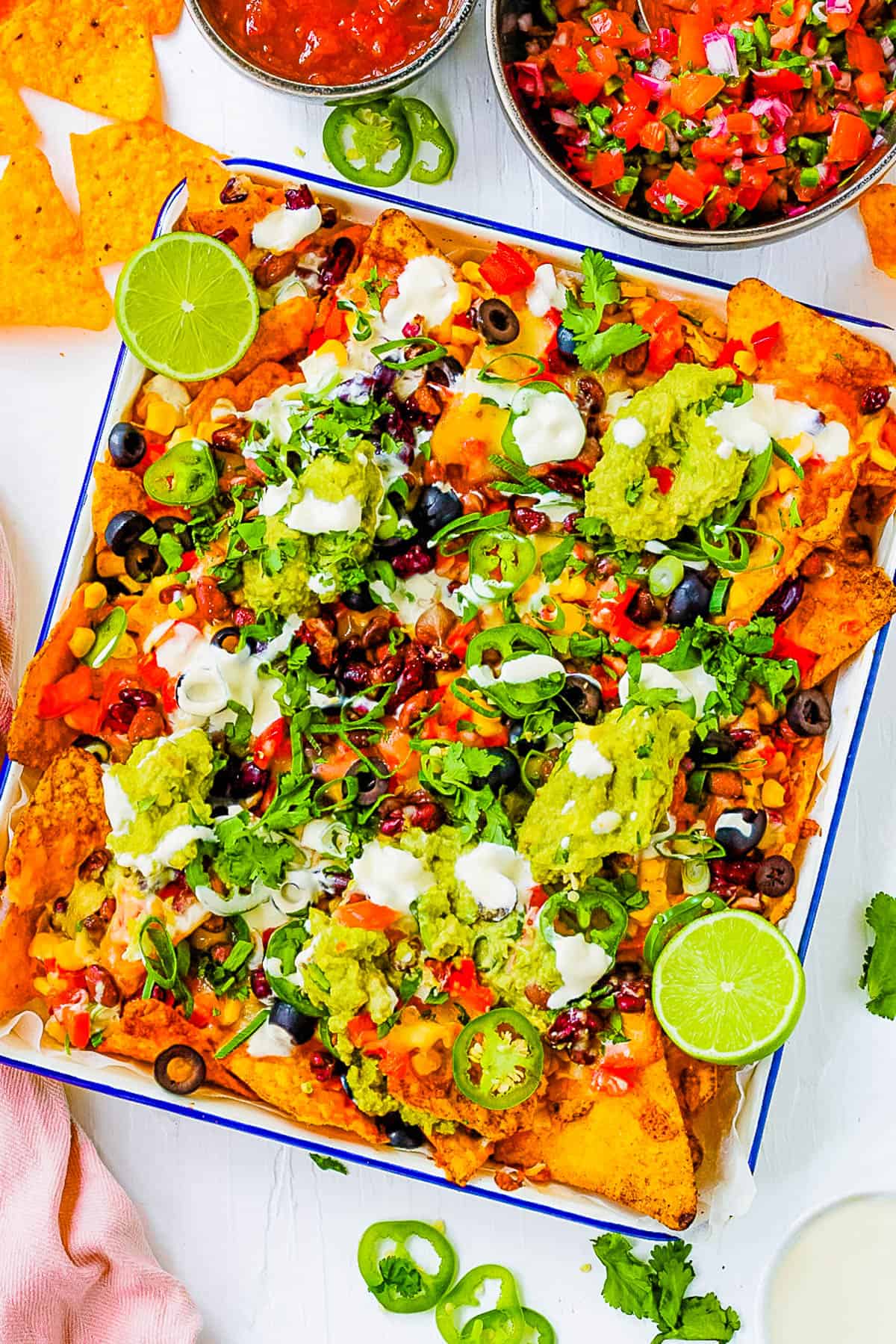 Loaded vegetarian nachos with veggies, jalapenos, guacamole, sour cream, cheese and olives served on a white platter.
