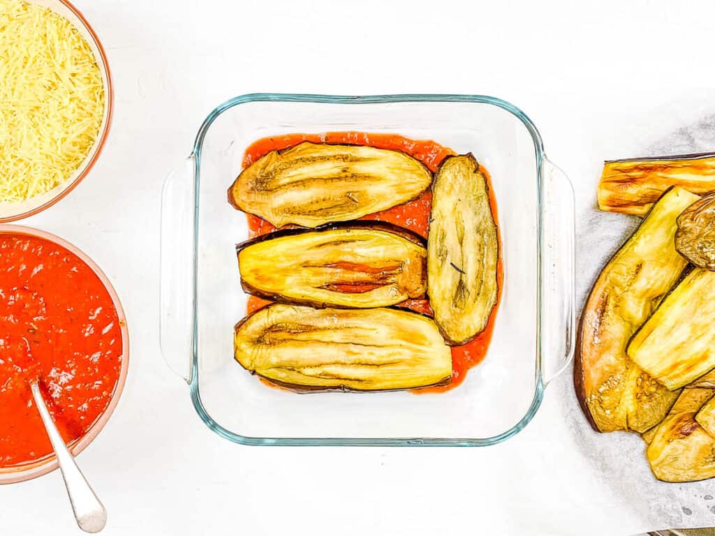 Eggplant slices and marinara sauce layered in a baking dish.