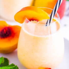Peach milk drink served in a glass with a straw, garnished with fresh peaches.