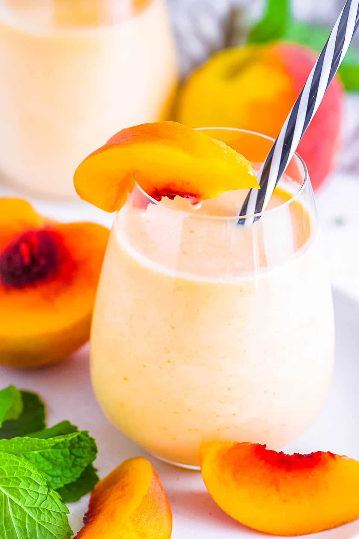 Peach milk drink served in a glass with a straw, garnished with fresh peaches.