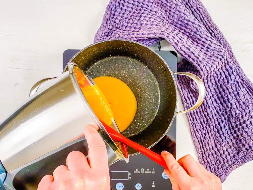 Peach puree being poured into a pot on the stove.