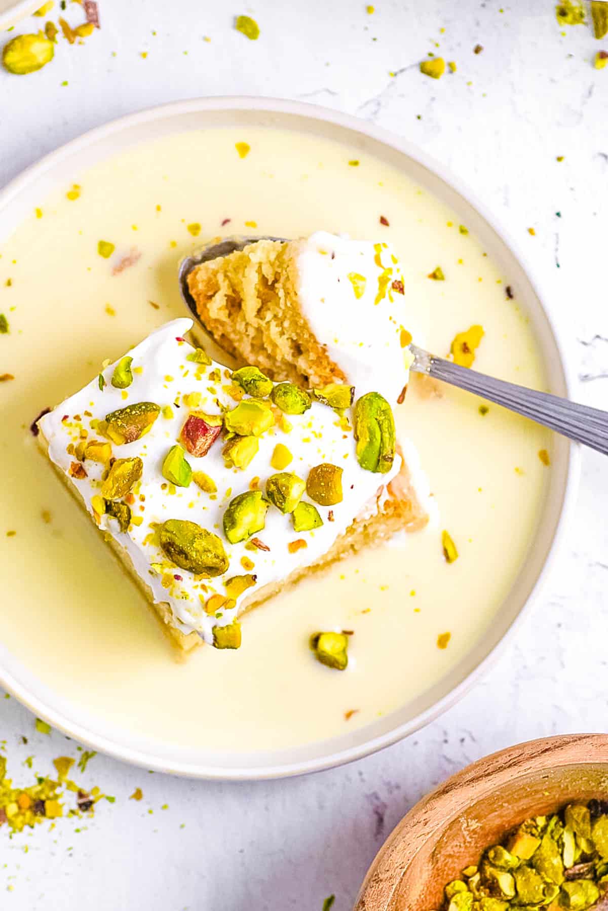 Rasmalai tres leches cake served on a white plate, topped with pistachios and the sweetened milk mixture.