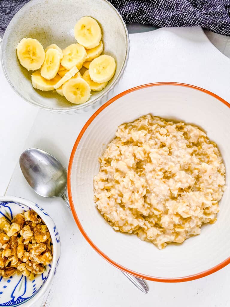 Cooked oatmeal in a bowl with toppings on the side.