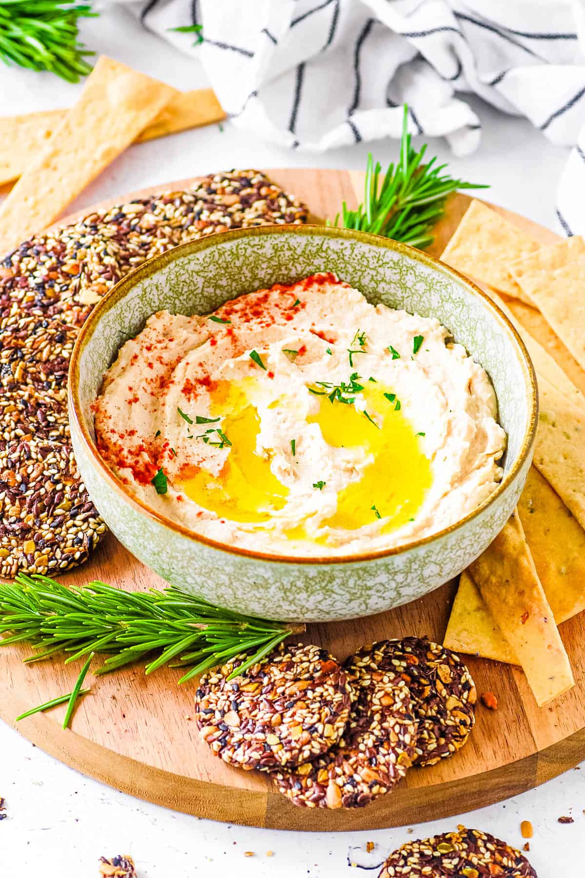 Healthy butter bean hummus served in a bowl, with olive oil drizzled on top and crackers on the side.