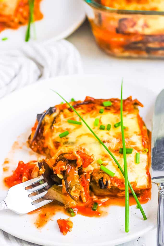 Slice of vegan eggplant parmesan served on a white plate with a fork.