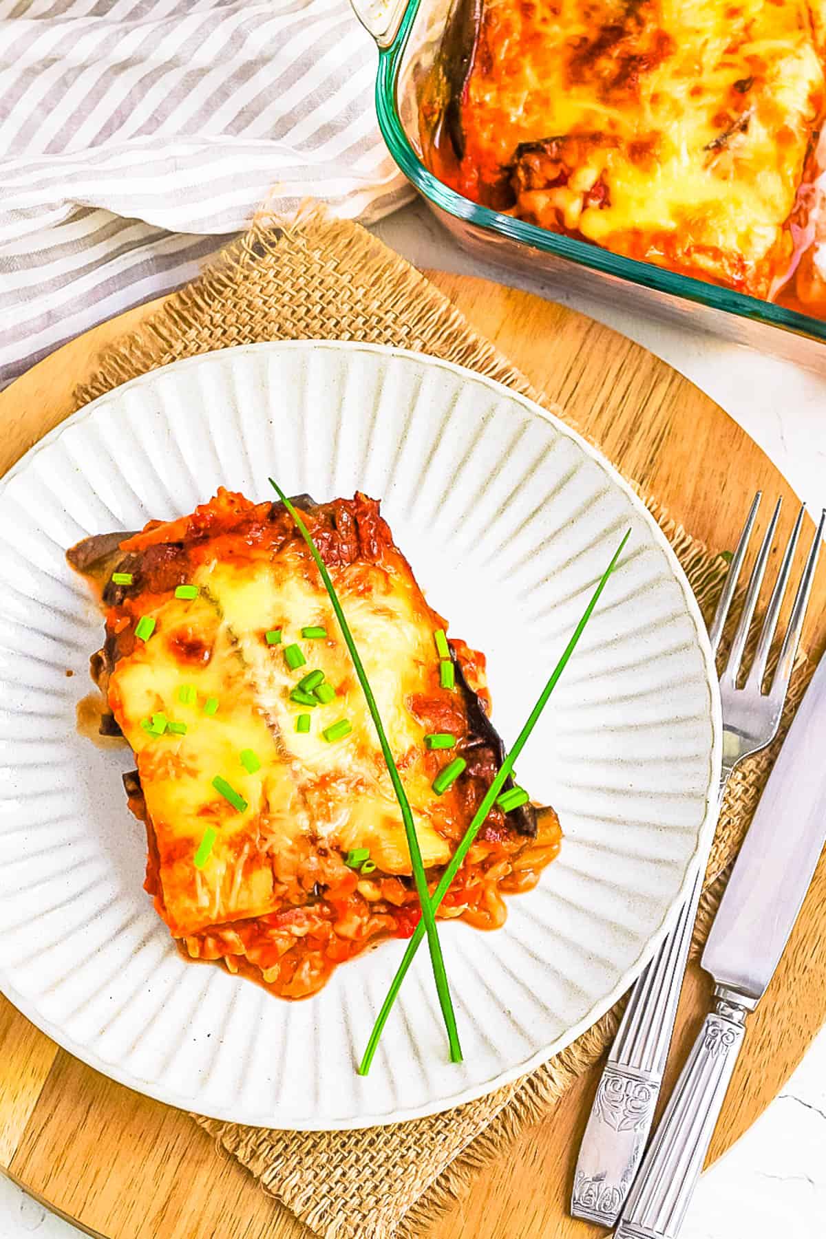 Vegan eggplant parmesan without breadcrumbs served on a white plate garnished with fresh herbs.