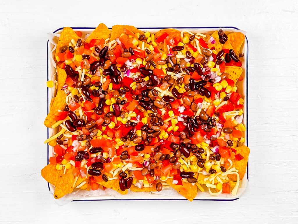 Tortilla chips topped with black beans and veggies on a baking sheet.