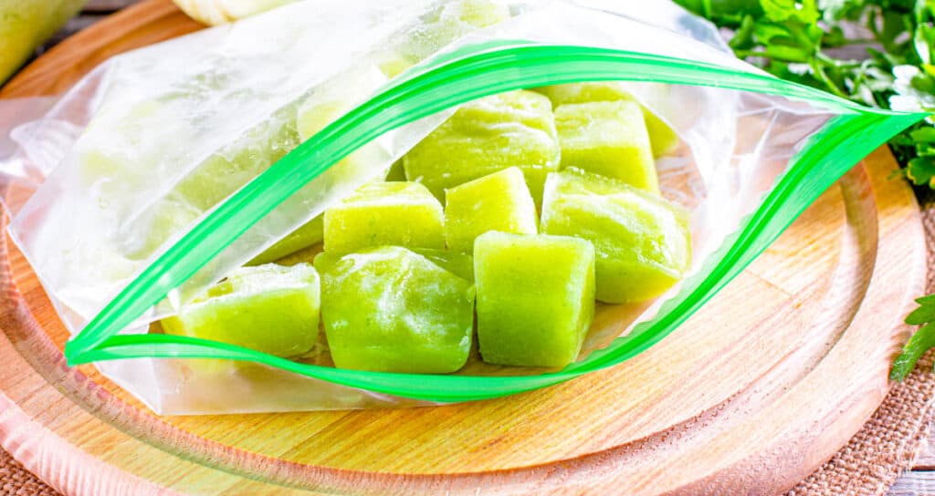 Frozen avocado baby food in ice cube shapes stored in a ziploc bag.