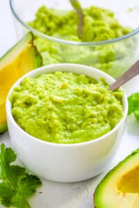 Avocado puree baby food served in a white bowl with a spoon.