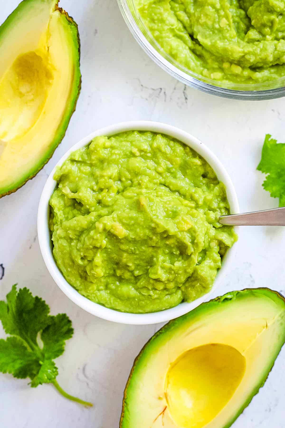 Avocado puree for baby served in a white bowl with a spoon.