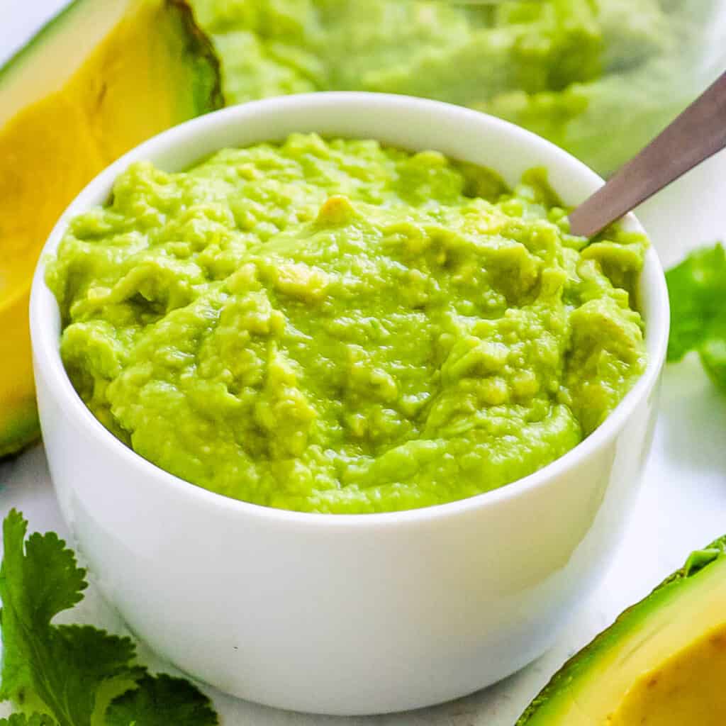 Stage 1 Avocado baby food served in a white bowl with a spoon.