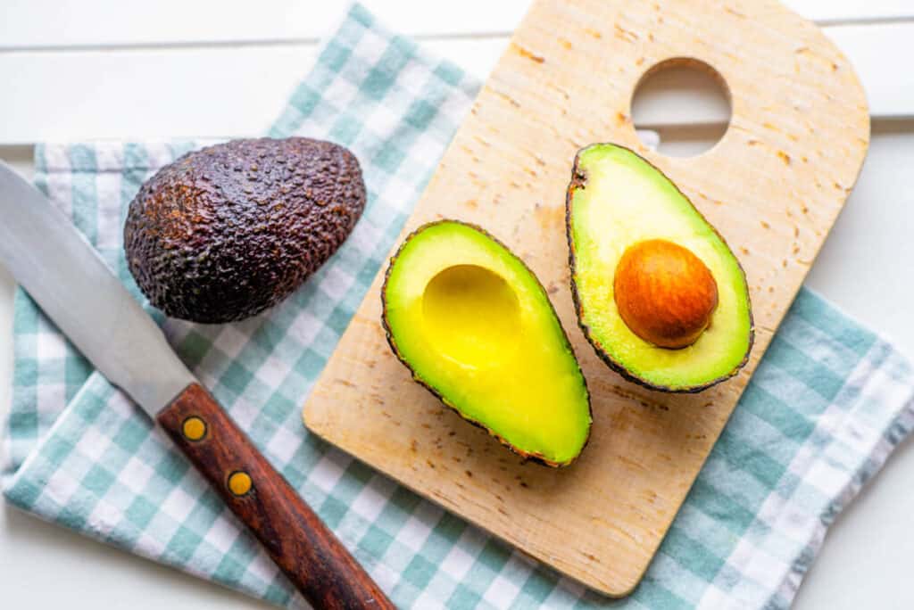 Fresh avocado halves on cutting board on white background.