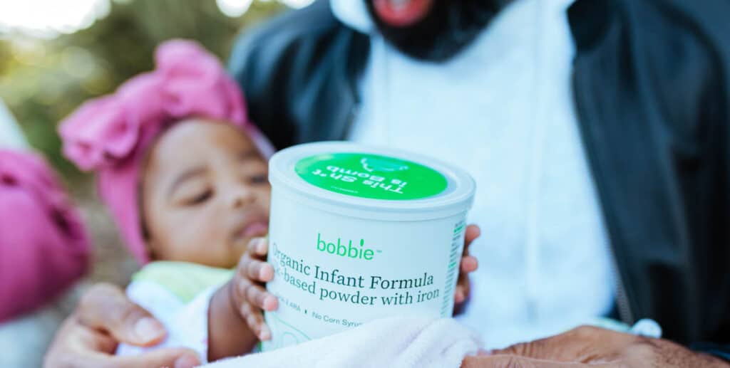 Can of Bobbie infant formula being held by a baby in her dad's arms.