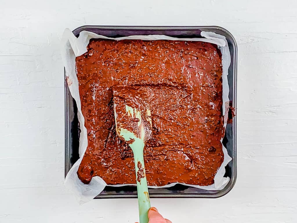 Breastfeeding brownies batter in a baking dish lined with parchment paper.