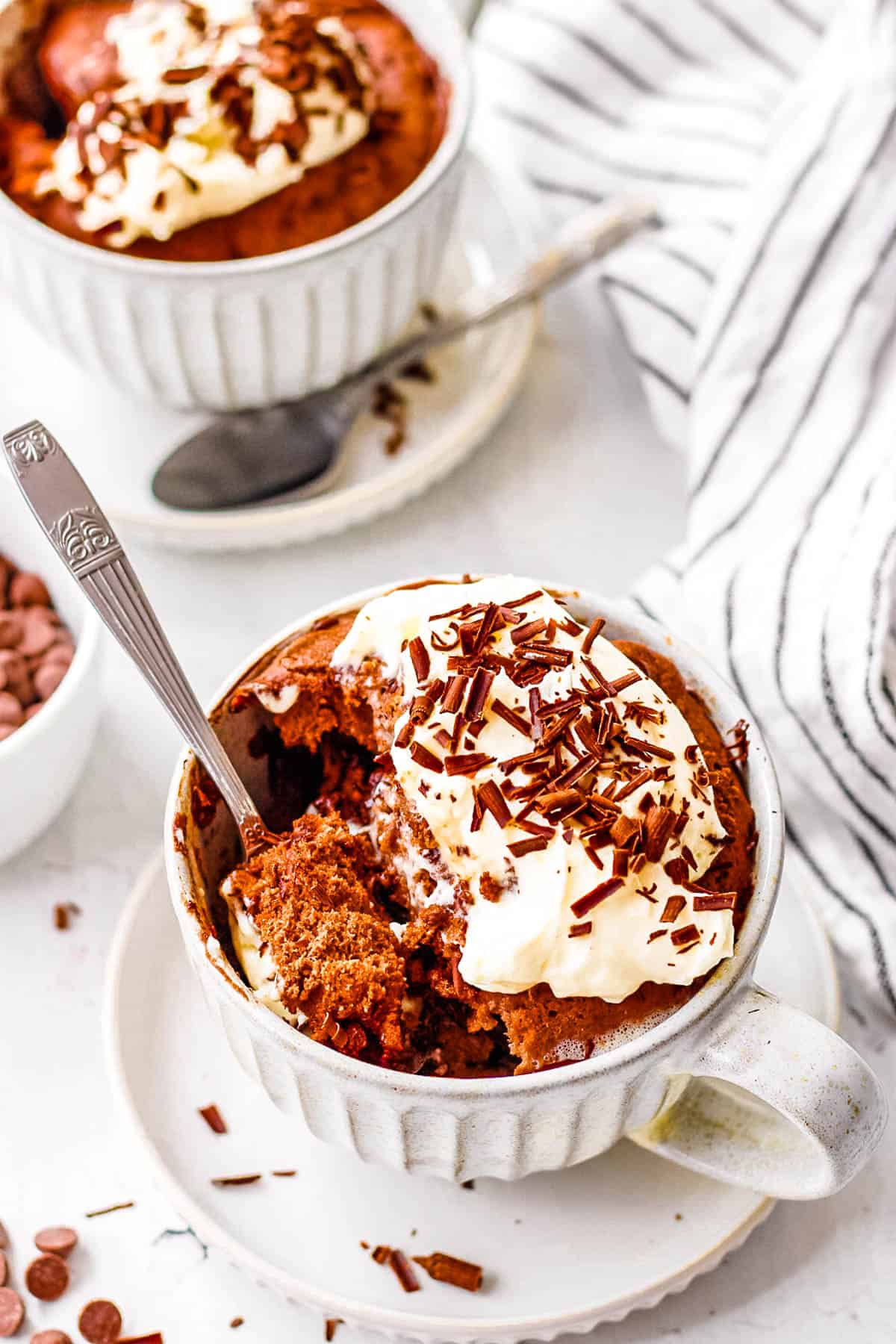 Chocolate protein powder mug cake served in a mug, topped with whipped cream and chocolate shavings.