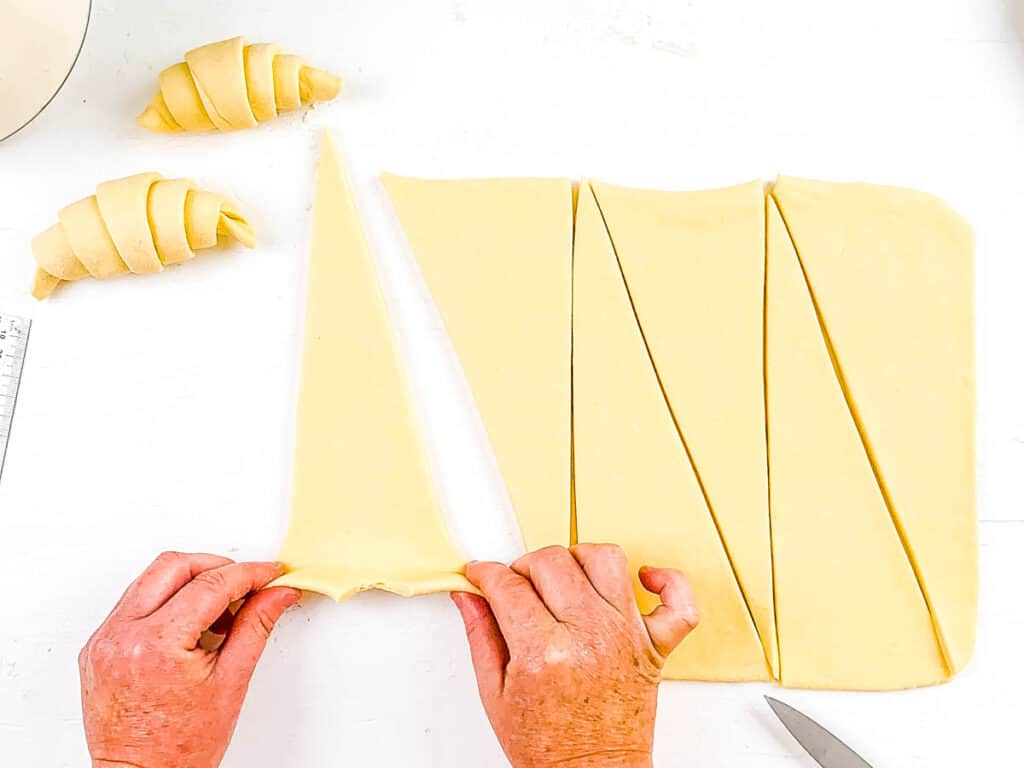 Croissant dough being cut into triangles, to prep for rolling into individual croissants.