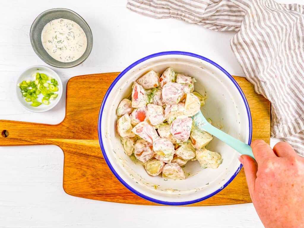 Stirring potato salad without eggs in a mixing bowl.