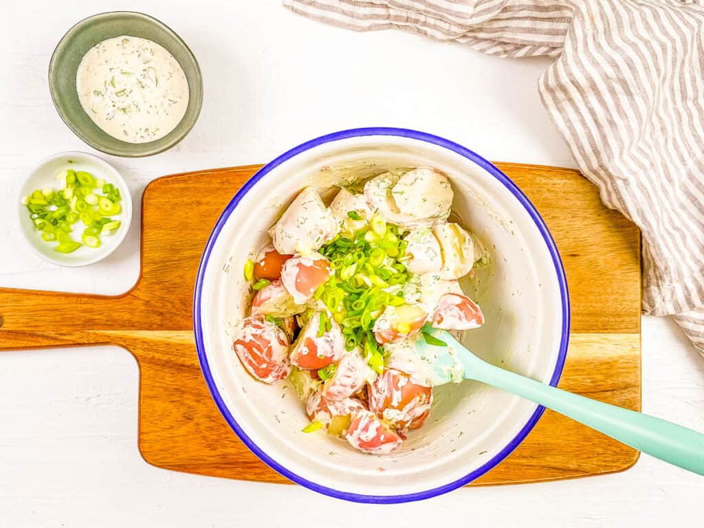 Healthy potato salad with green onions and no eggs in a mixing bowl.