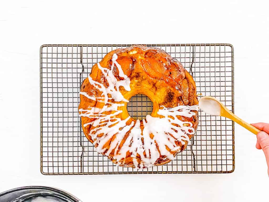 Fresh peach cobbler bundt cake on a wire rack with icing drizzled over the top.
