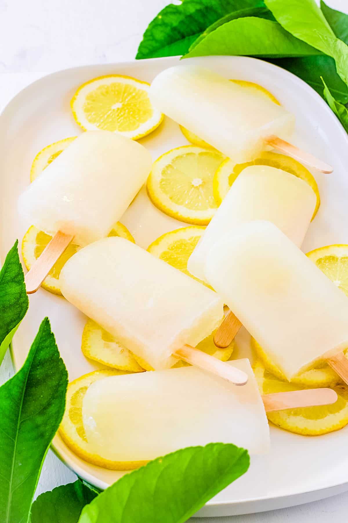 Hausgemachtes Limonadeneis am Stiel auf einem weißen Tablett mit Zitronenscheiben als Garnierung.
