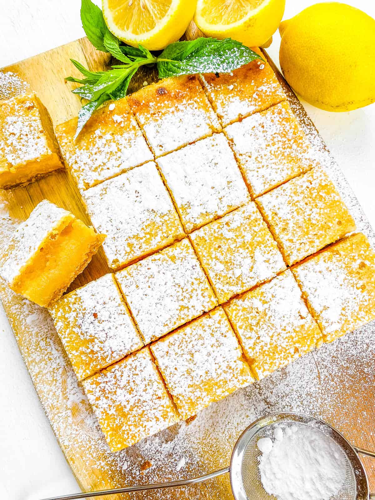 Gluten free lemon bars with graham cracker crust cut into squares on a cutting board.