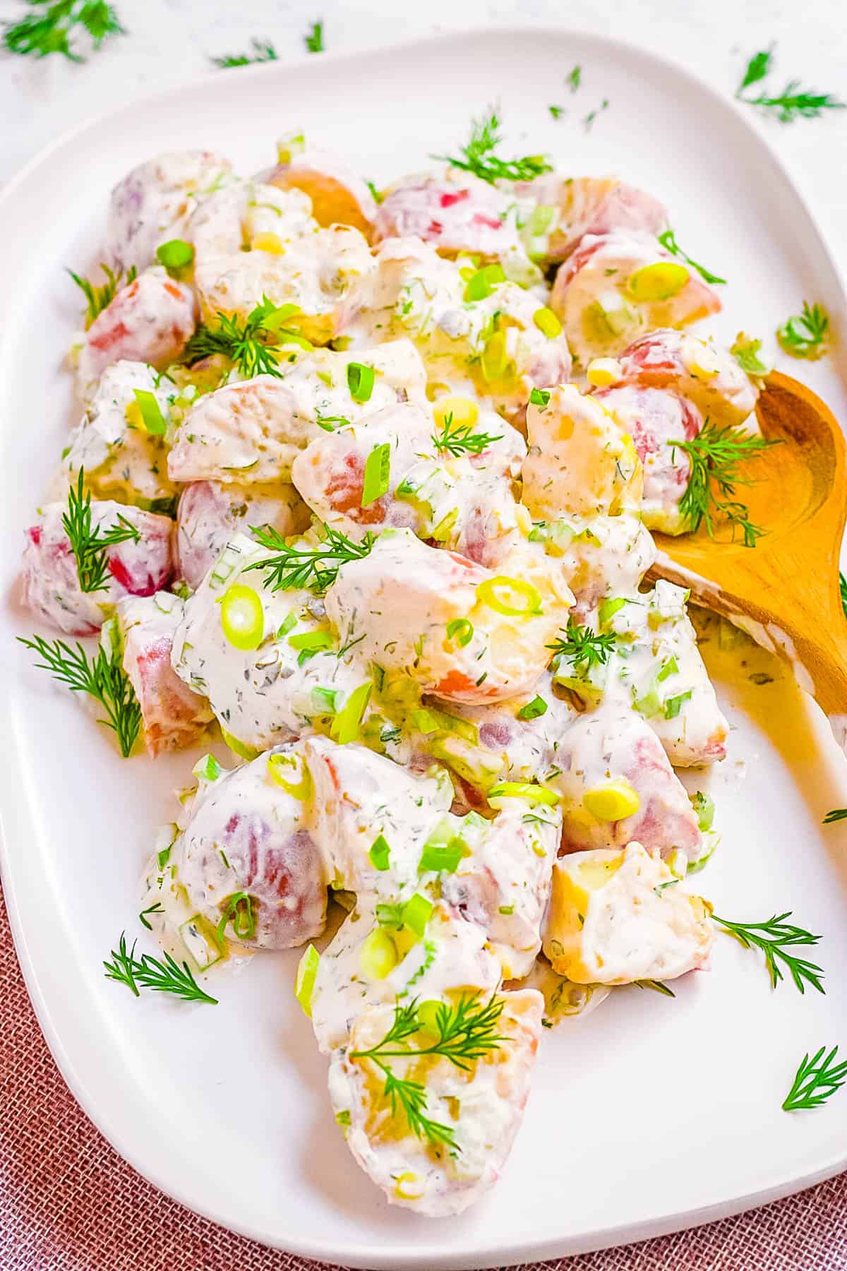 Easy potato salad without eggs served on a white plate with a wooden spoon.