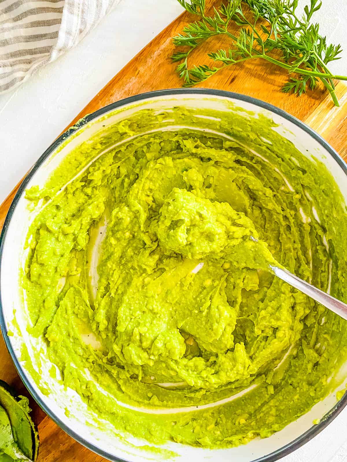 Mashed avocado in a white bowl with a spoon.