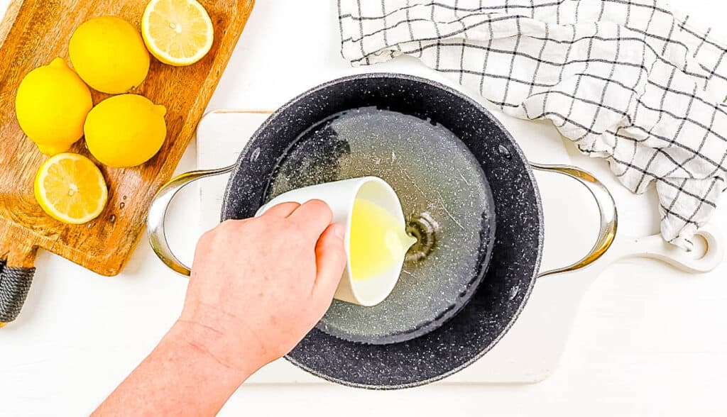 Jus de citron ajouté au sucre et à l'eau dans une casserole sur la cuisinière.
