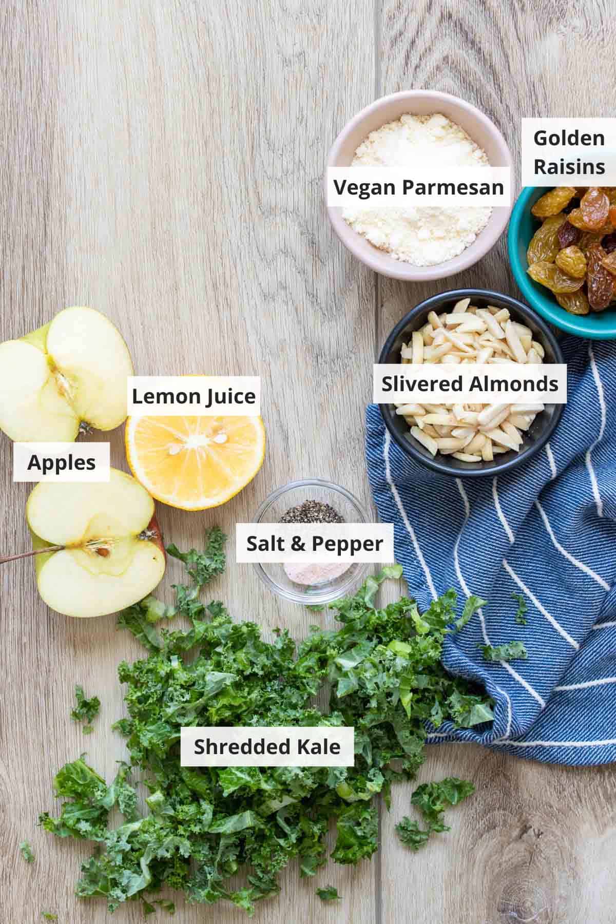 Ingredients for a vegan kale salad with lemon dressing on a light wood background.