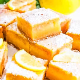 Lemon bars with graham cracker crust stacked on parchment paper.