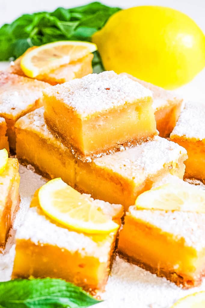 Lemon bars with graham cracker crust stacked on parchment paper.