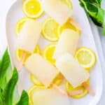 Lemon popsicles on a white tray with lemon slices as a garnish.