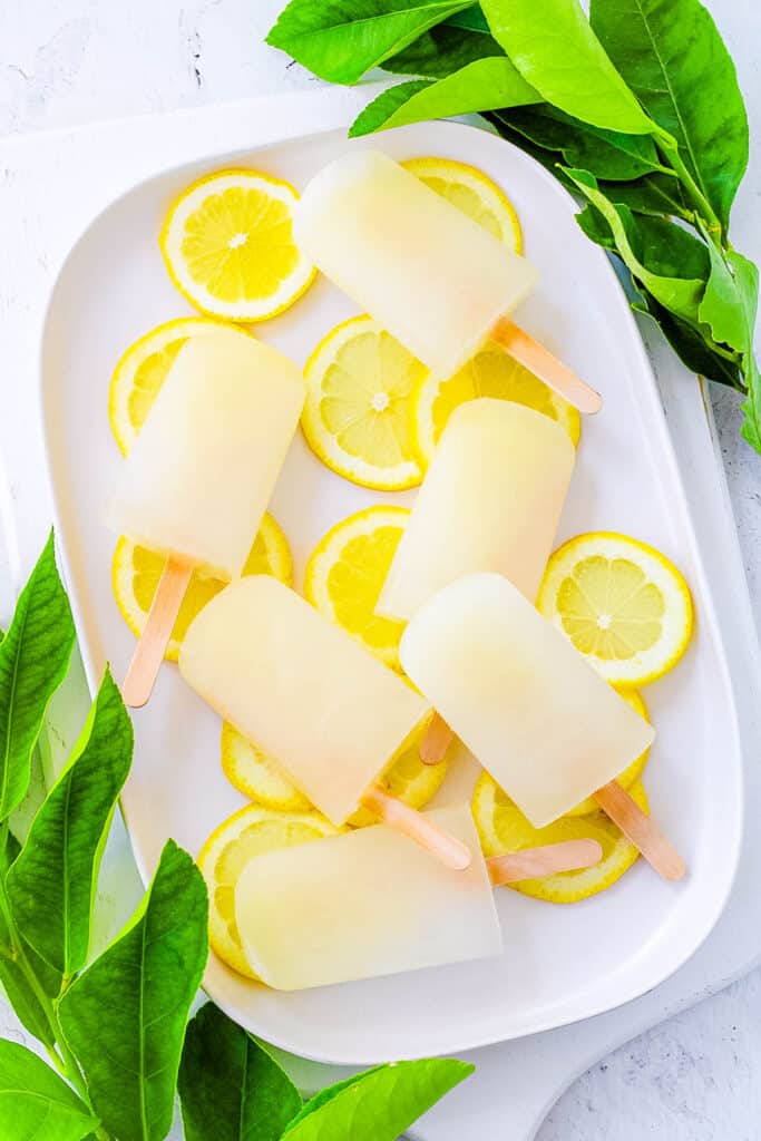 Lemon popsicles on a white tray with lemon slices as a garnish.