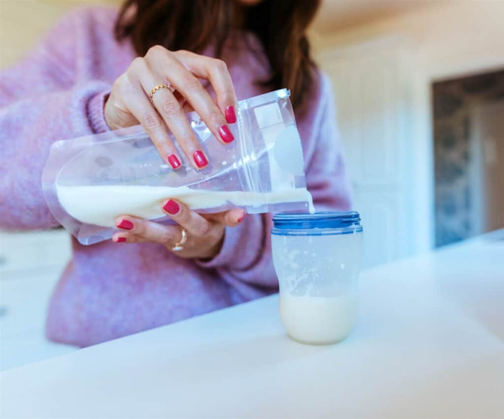 Woman mixing baby formula in a plastic container and pouring it into a bottle.