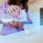 Woman mixing baby formula in a plastic container and pouring it into a bottle.