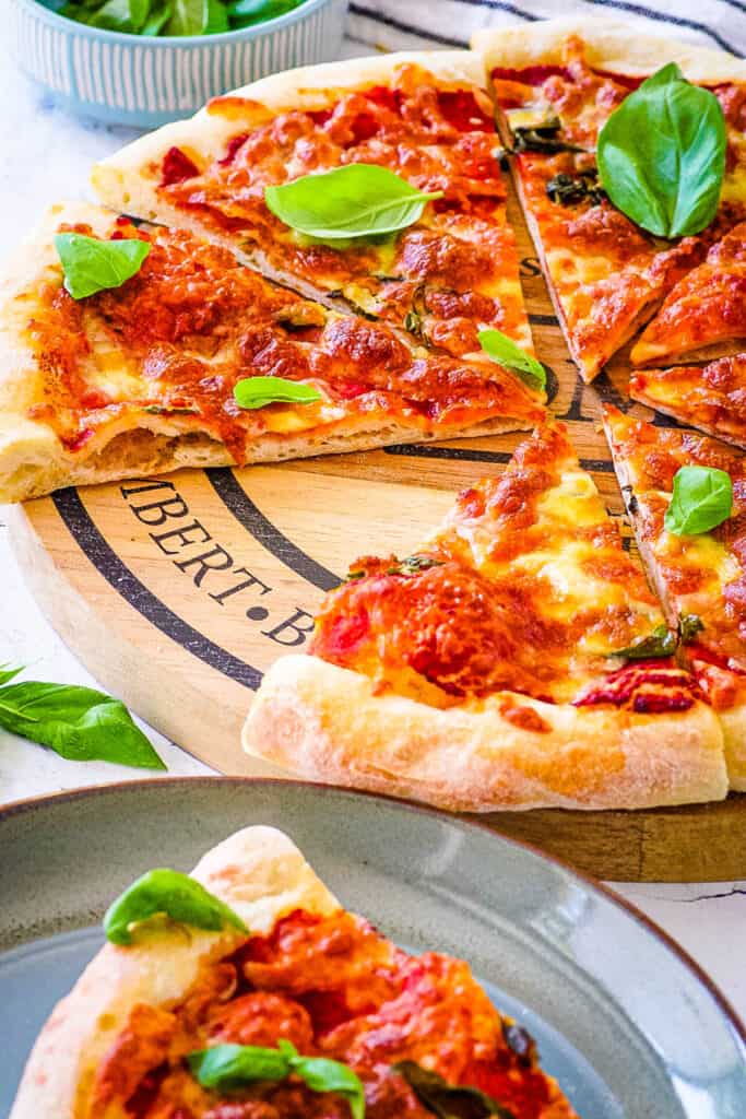 Poolish pizza dough topped with tomatoes and basil, baked in the oven and served on a wooden cutting board.