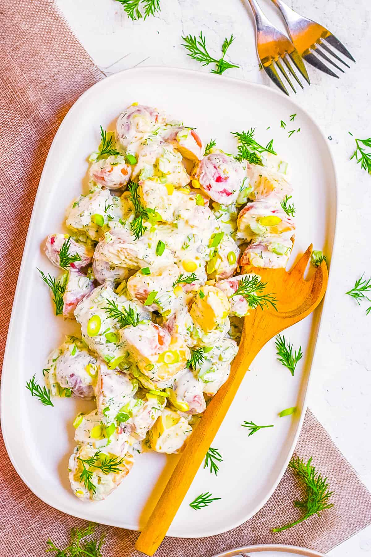 Overhead shot of a white serving dish of healthy potato salad with a wooden spoon.