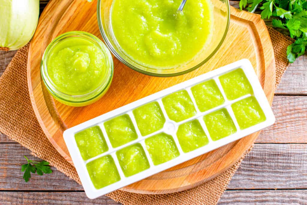 Baby food avocado stored in ice cube trays, ready for freezing on a cutting board.